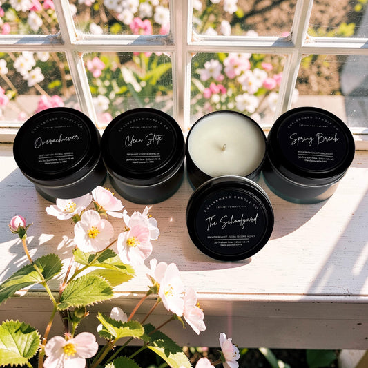 Five scented candles on a windowsill with flowers in the foreground